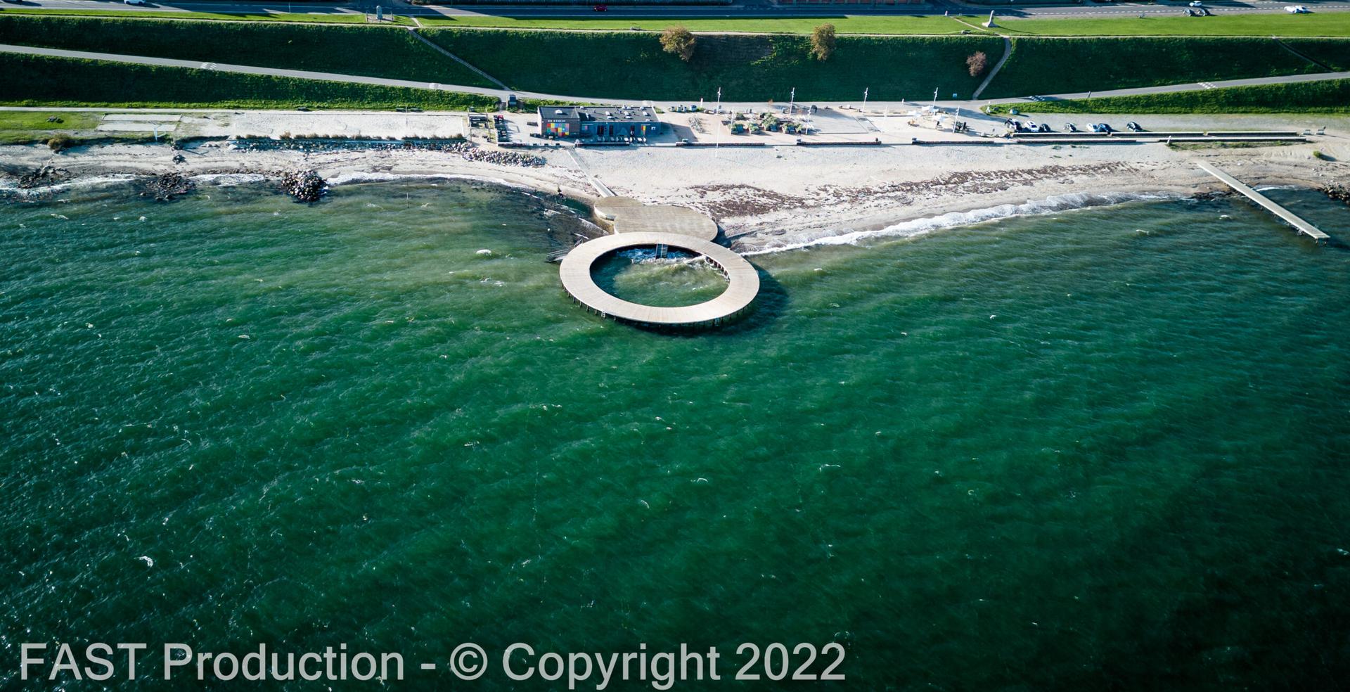 Luftfoto af strandpromenade og cirkulær badebro set fra havet