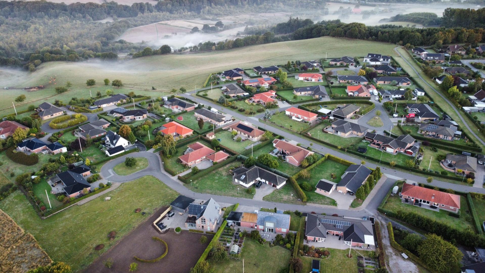 Dronefoto af nyt boligområde ved solopgang med morgentåge over markerne bagved