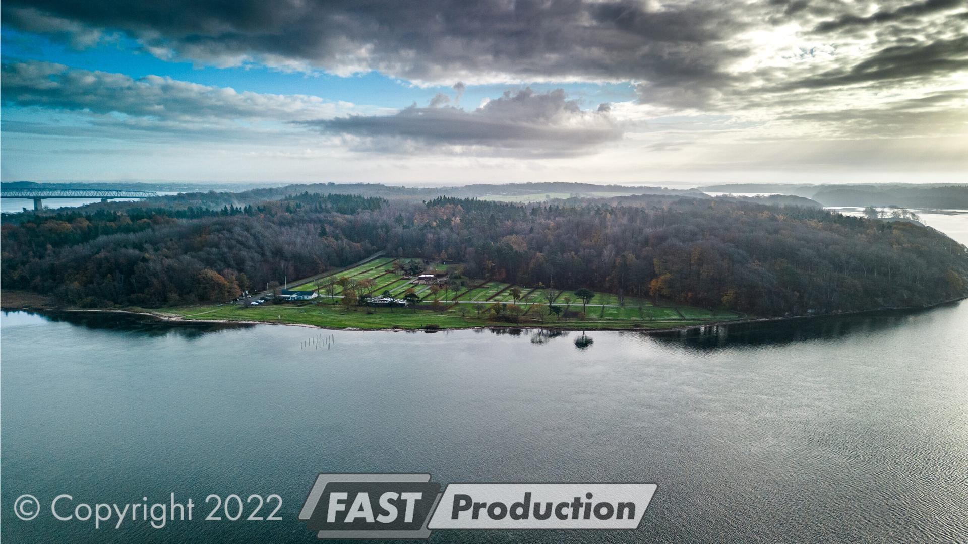 Dronefoto af skovklædte Galsklint ved Lillebælt under dramatiske skyer, Lillebæltsbroerne i det fjerne