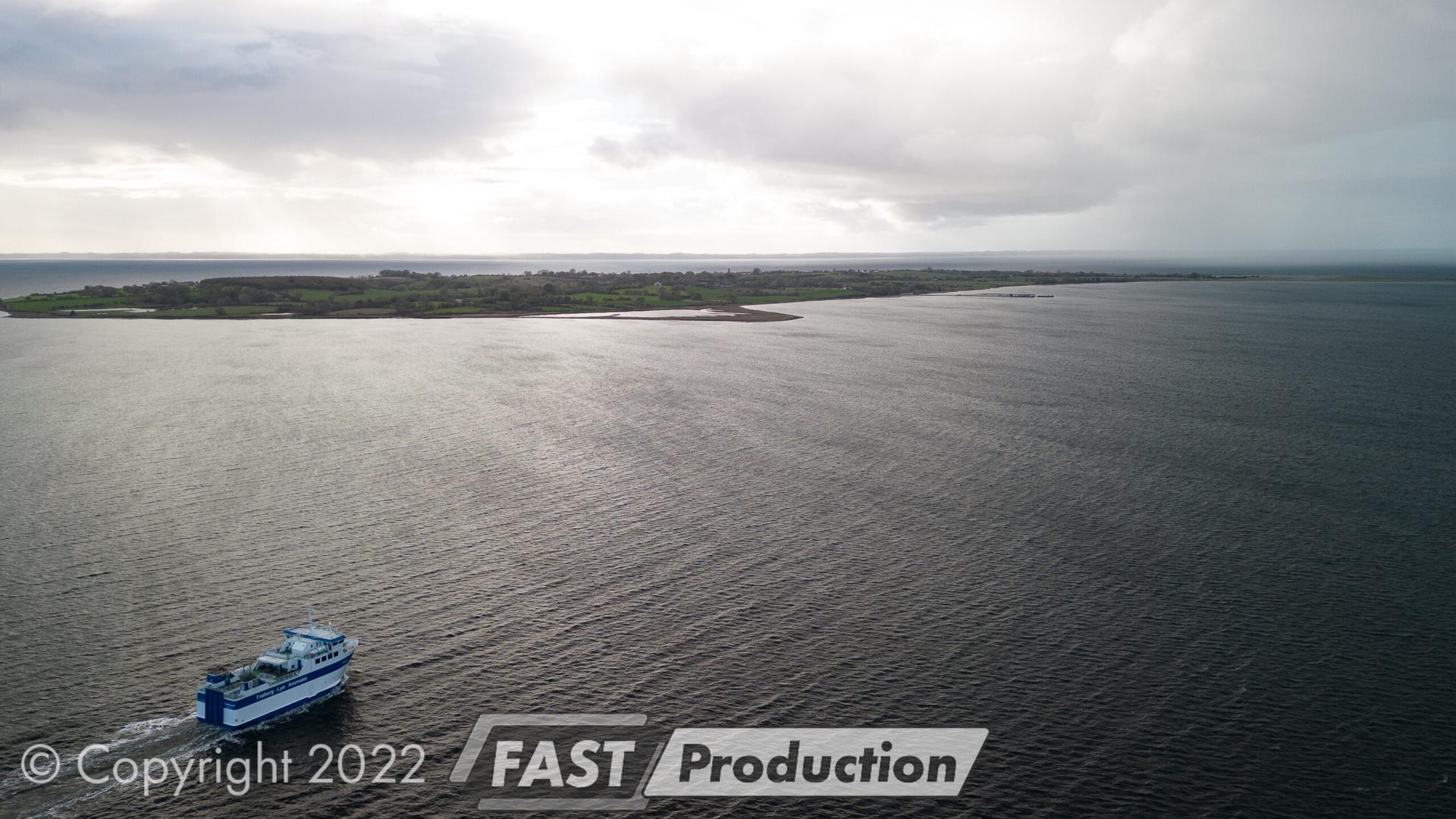 Uredigeret dronefoto af Lyø-færgen med grå himmel og flade farver
